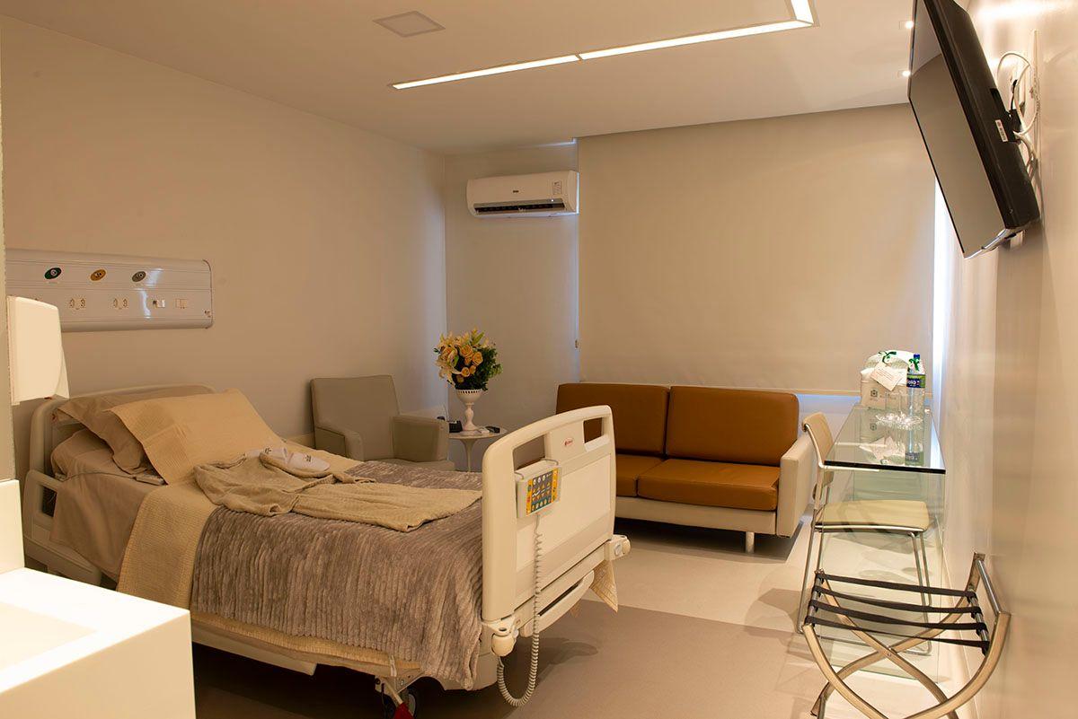 Quarto hospitalar confortável com cama ajustável, sofá, TV e decoração simples, criando um ambiente acolhedor para pacientes.