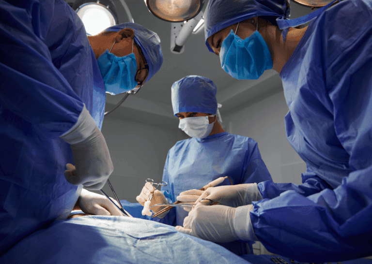 Equipe médica realizando cirurgia em ambiente esterilizado, todos usando máscaras, luvas e roupas cirúrgicas."